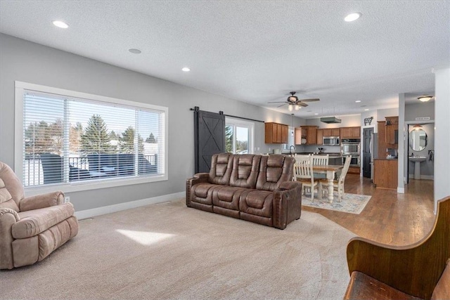 living room with a textured ceiling, a barn door, recessed lighting, a ceiling fan, and baseboards