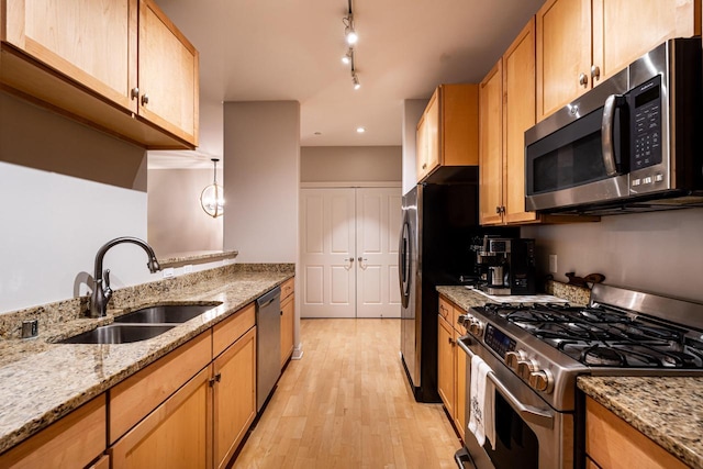 kitchen featuring light stone counters, rail lighting, light wood-style flooring, appliances with stainless steel finishes, and a sink