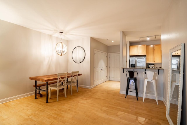 kitchen with light wood finished floors, a kitchen bar, light brown cabinetry, stainless steel fridge, and baseboards