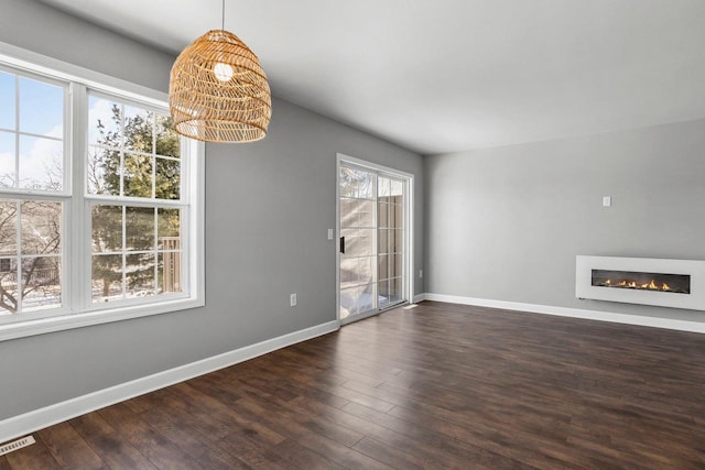 unfurnished dining area with visible vents, baseboards, wood finished floors, and a glass covered fireplace