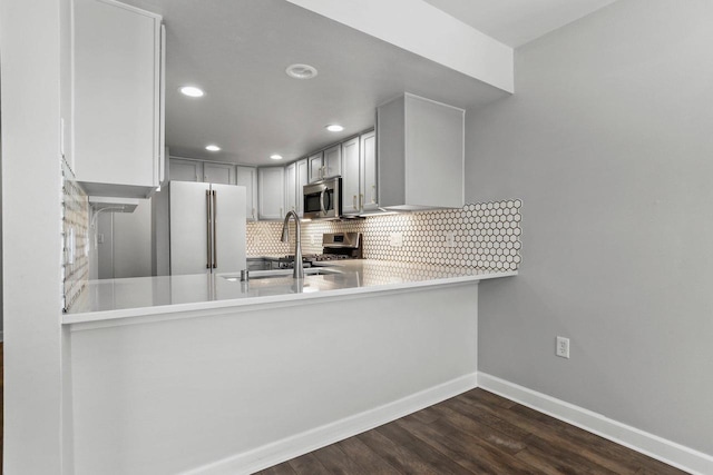 kitchen featuring baseboards, decorative backsplash, dark wood-style floors, stainless steel microwave, and freestanding refrigerator