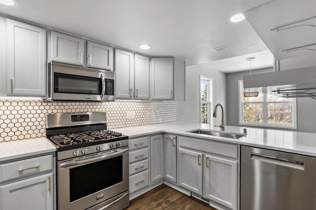 kitchen featuring gray cabinetry, stainless steel appliances, a sink, light countertops, and tasteful backsplash