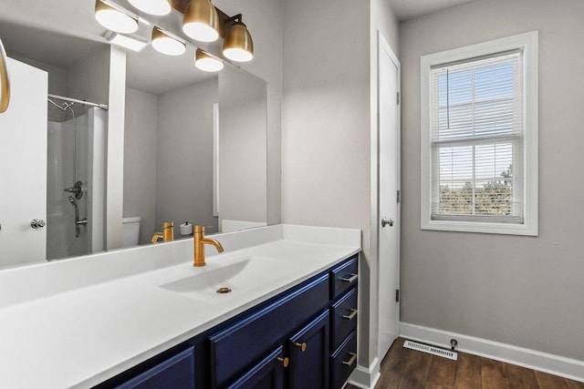 bathroom featuring toilet, wood finished floors, vanity, baseboards, and walk in shower