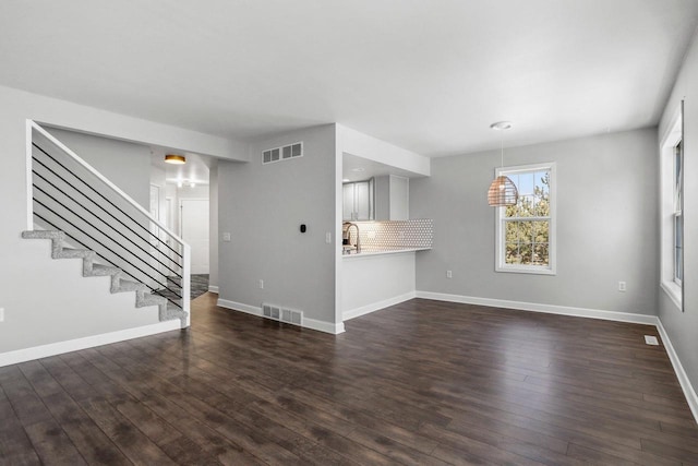 unfurnished living room with dark wood-style floors, baseboards, stairs, and visible vents