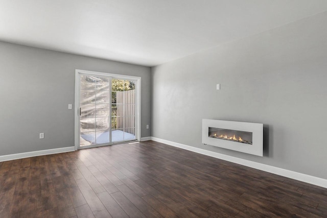 unfurnished living room featuring dark wood-type flooring, a glass covered fireplace, and baseboards