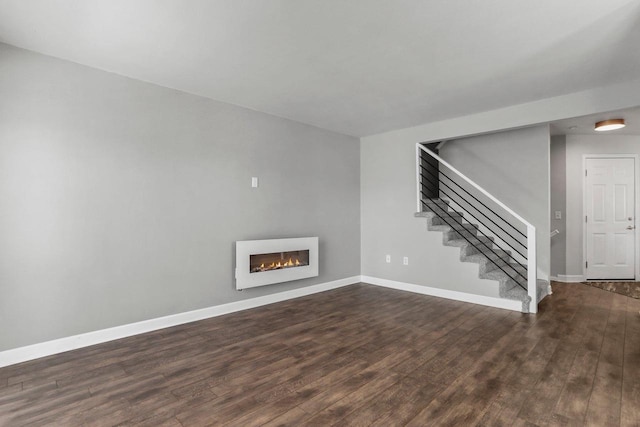 unfurnished living room with a glass covered fireplace, wood finished floors, baseboards, and stairs