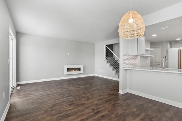 unfurnished living room featuring dark wood-style flooring, a lit fireplace, and baseboards