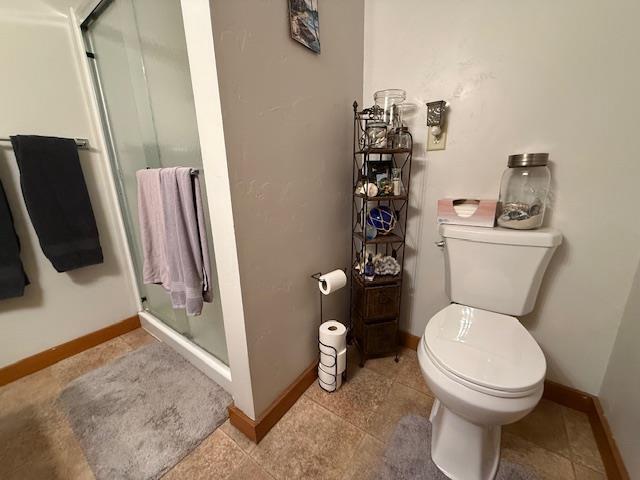 bathroom with toilet, a stall shower, and baseboards