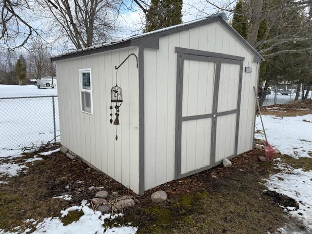 snow covered structure featuring a shed, fence, and an outdoor structure