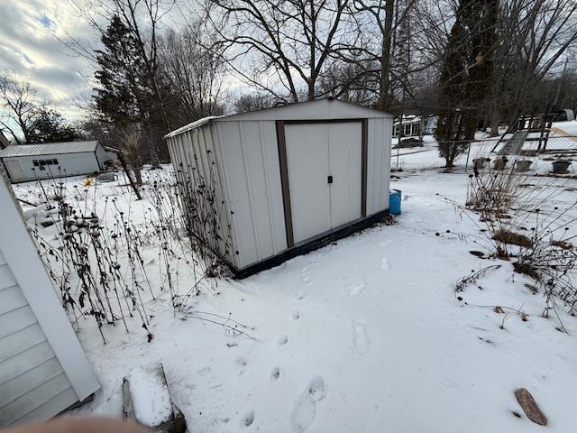 snow covered structure with a storage shed and an outbuilding