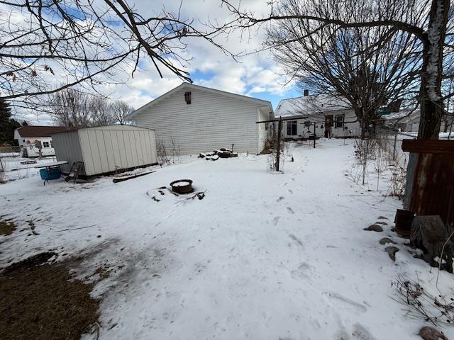 yard covered in snow featuring a detached garage, a storage unit, and an outbuilding