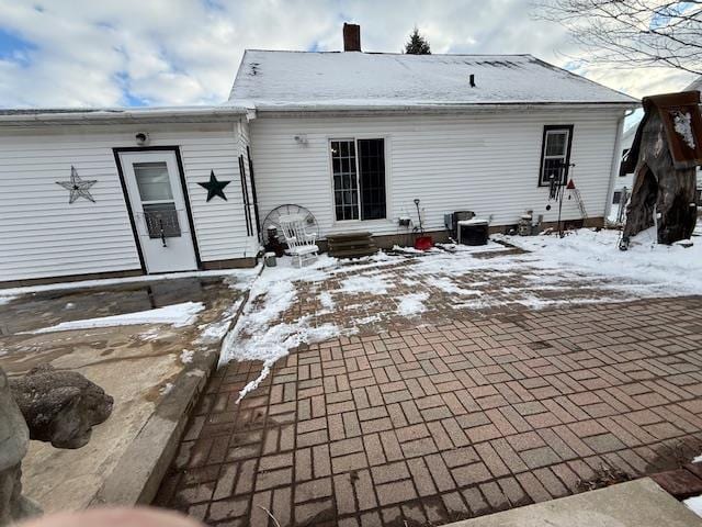 snow covered back of property featuring a chimney and a patio area