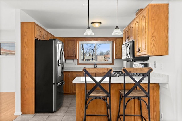 kitchen featuring light tile patterned flooring, a peninsula, light countertops, appliances with stainless steel finishes, and pendant lighting