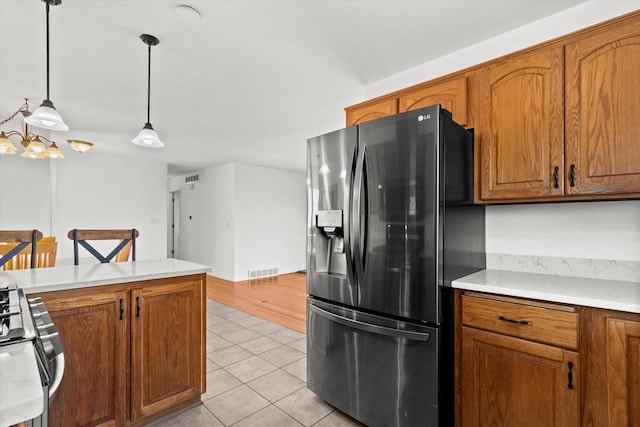 kitchen with stainless steel appliances, brown cabinetry, light tile patterned flooring, and visible vents