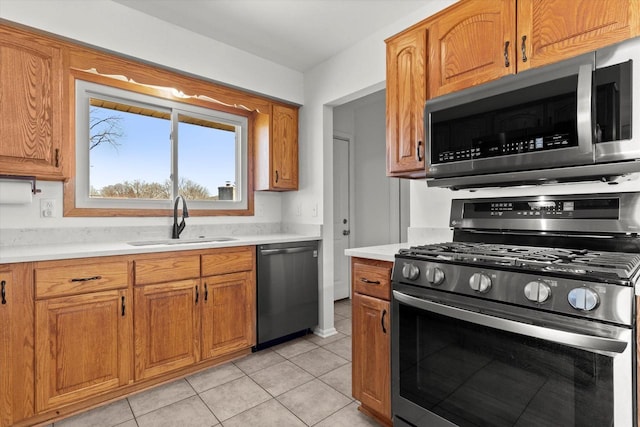 kitchen featuring light tile patterned floors, a sink, light countertops, appliances with stainless steel finishes, and brown cabinets