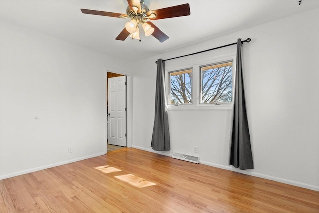 empty room featuring a ceiling fan, light wood-type flooring, visible vents, and baseboards