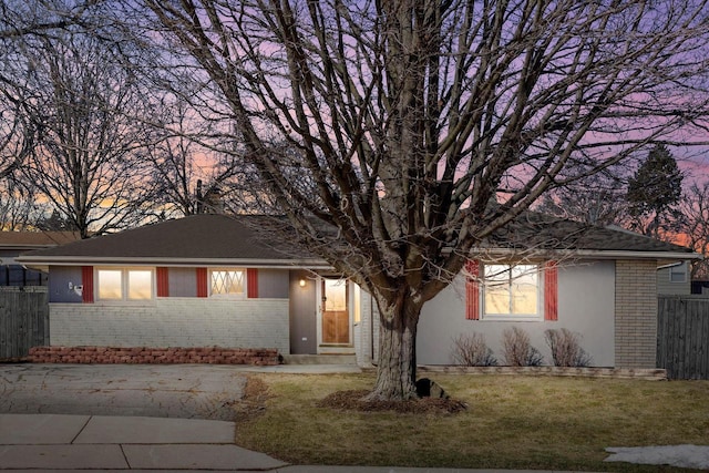 ranch-style home featuring a yard, brick siding, and fence