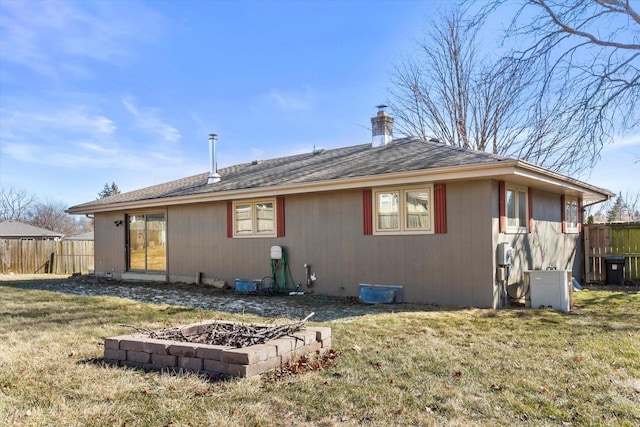 rear view of house with a fire pit, a chimney, fence, and a lawn