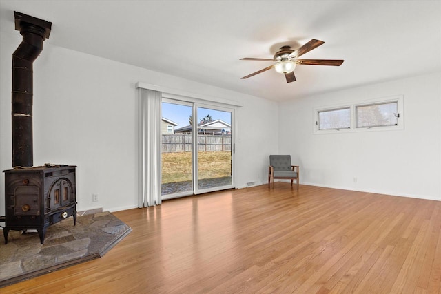 living area with visible vents, baseboards, ceiling fan, wood finished floors, and a wood stove