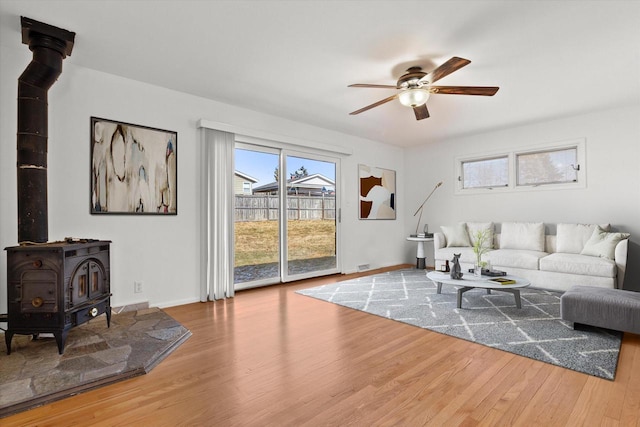 living area featuring baseboards, wood finished floors, a wood stove, and a ceiling fan