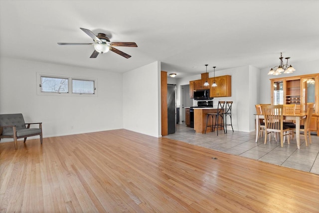 living area featuring light wood-style floors, baseboards, a wealth of natural light, and ceiling fan with notable chandelier