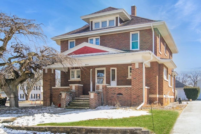 american foursquare style home with brick siding, a chimney, and a porch