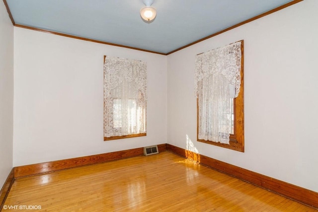 spare room with ornamental molding, wood-type flooring, visible vents, and baseboards