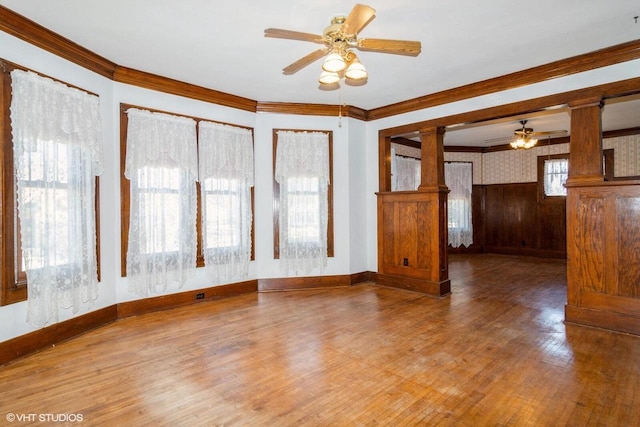 spare room with crown molding, wood finished floors, a wealth of natural light, and ornate columns