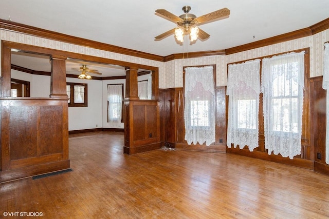 unfurnished living room with wood finished floors, ornate columns, and wallpapered walls