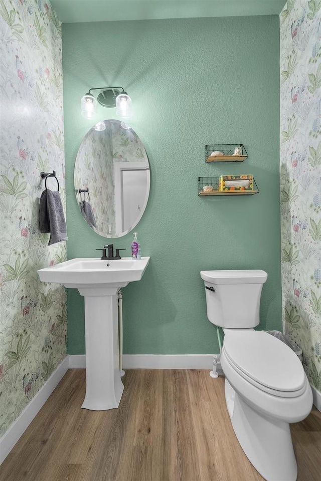 bathroom featuring toilet, wallpapered walls, baseboards, and wood finished floors