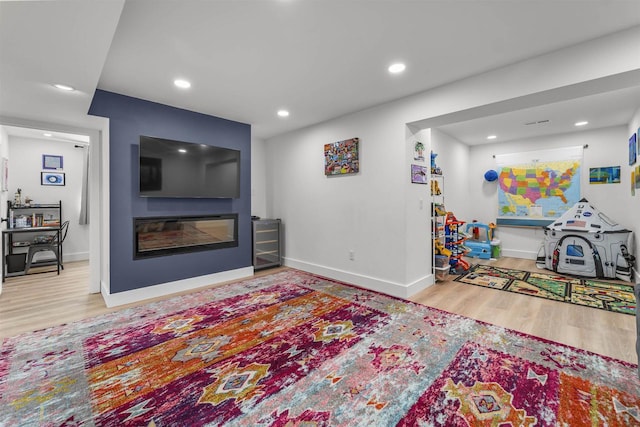 playroom featuring baseboards, a glass covered fireplace, wood finished floors, and recessed lighting