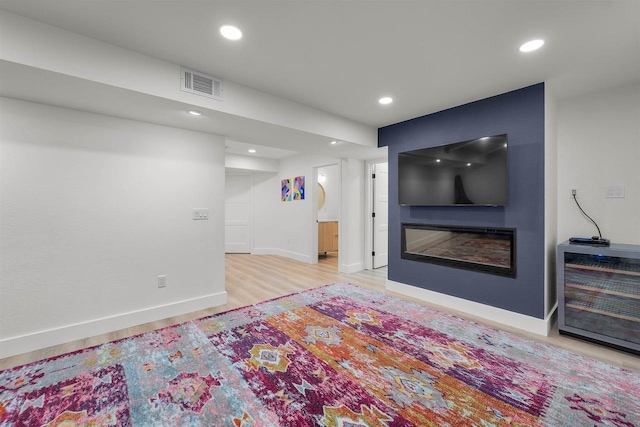 living area featuring light wood finished floors, a glass covered fireplace, visible vents, and recessed lighting