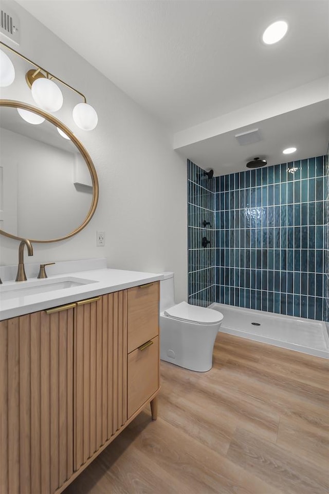 bathroom with visible vents, toilet, wood finished floors, a tile shower, and vanity