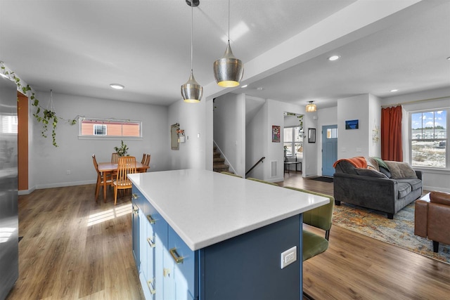 kitchen featuring wood finished floors, open floor plan, light countertops, blue cabinetry, and a center island