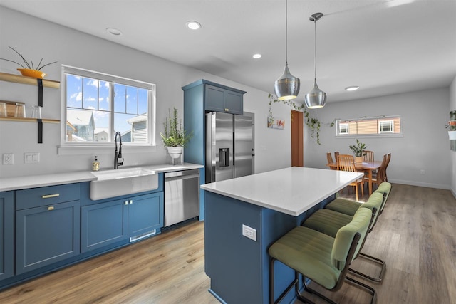 kitchen featuring a breakfast bar, blue cabinetry, appliances with stainless steel finishes, a sink, and a kitchen island