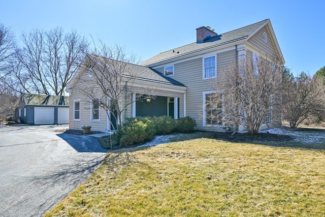 view of front of property with a garage, a chimney, an outdoor structure, and a front lawn