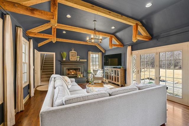 living room featuring wood finished floors, vaulted ceiling with beams, recessed lighting, a warm lit fireplace, and a notable chandelier