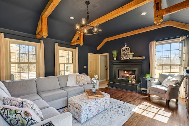 living room with lofted ceiling with beams, wood finished floors, a warm lit fireplace, and a chandelier