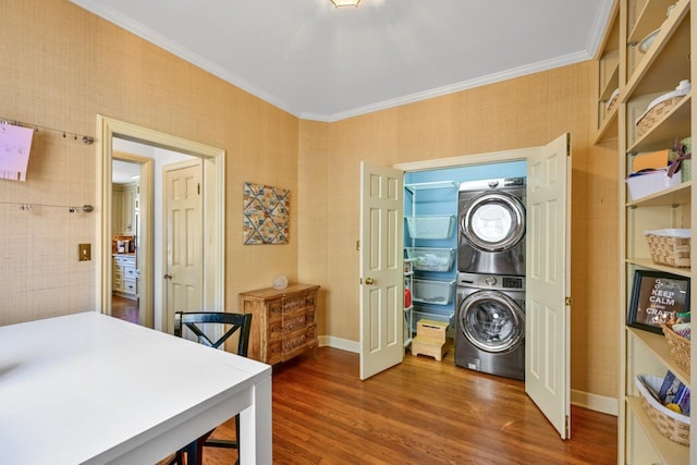 clothes washing area featuring baseboards, stacked washer and clothes dryer, wood finished floors, and crown molding