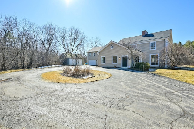 view of front of house featuring an outbuilding, curved driveway, a chimney, and a garage