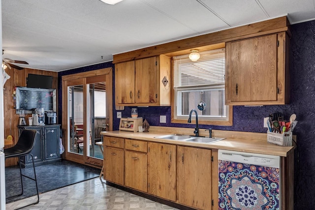 kitchen featuring brown cabinets, white dishwasher, light countertops, light floors, and a sink