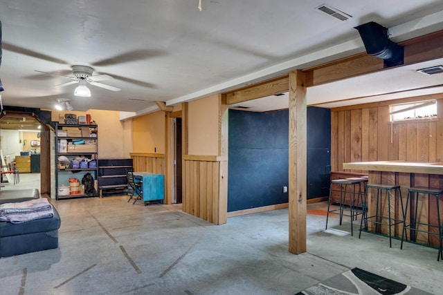 below grade area with a wainscoted wall, a dry bar, wood walls, and visible vents