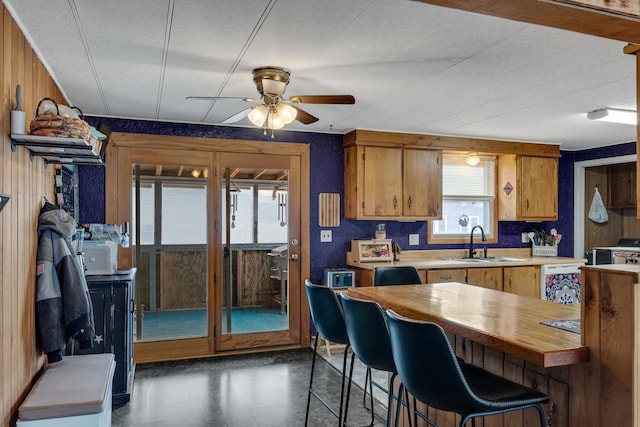 kitchen featuring brown cabinetry, a ceiling fan, wood walls, wooden counters, and a sink