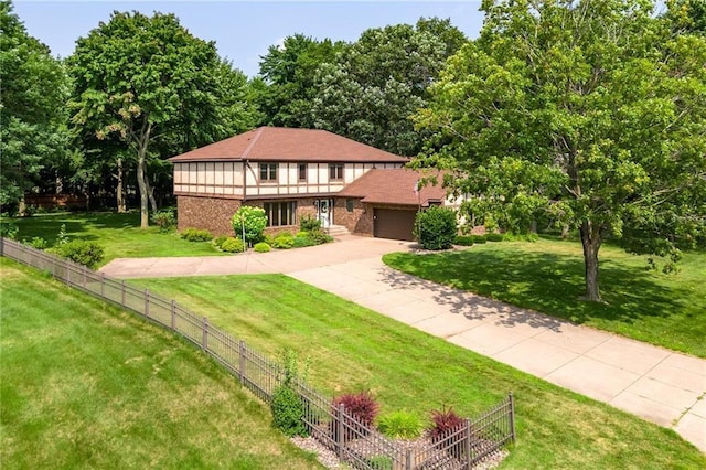 tudor house with a garage, fence, concrete driveway, and a front yard