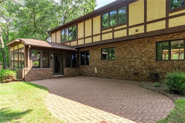 rear view of property featuring a patio, brick siding, a sunroom, and stucco siding