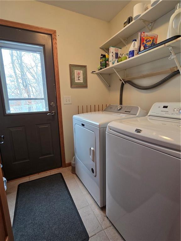 clothes washing area featuring laundry area, washer and clothes dryer, and light tile patterned floors