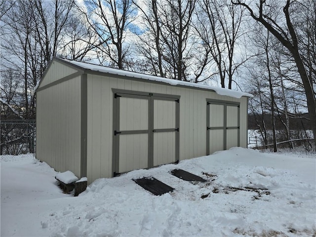 snow covered structure with an outbuilding, a storage shed, and fence