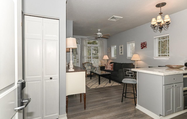 interior space featuring visible vents, a breakfast bar area, dark wood-style flooring, gray cabinetry, and ceiling fan with notable chandelier