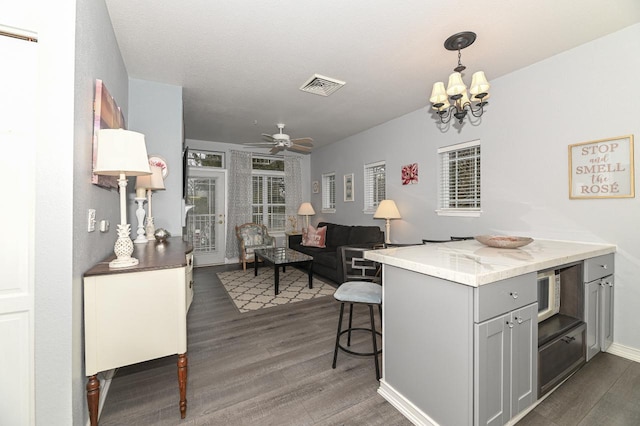 kitchen with decorative light fixtures, dark wood finished floors, visible vents, a kitchen bar, and ceiling fan with notable chandelier