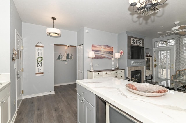 kitchen with baseboards, a tile fireplace, dark wood-type flooring, decorative light fixtures, and light stone countertops